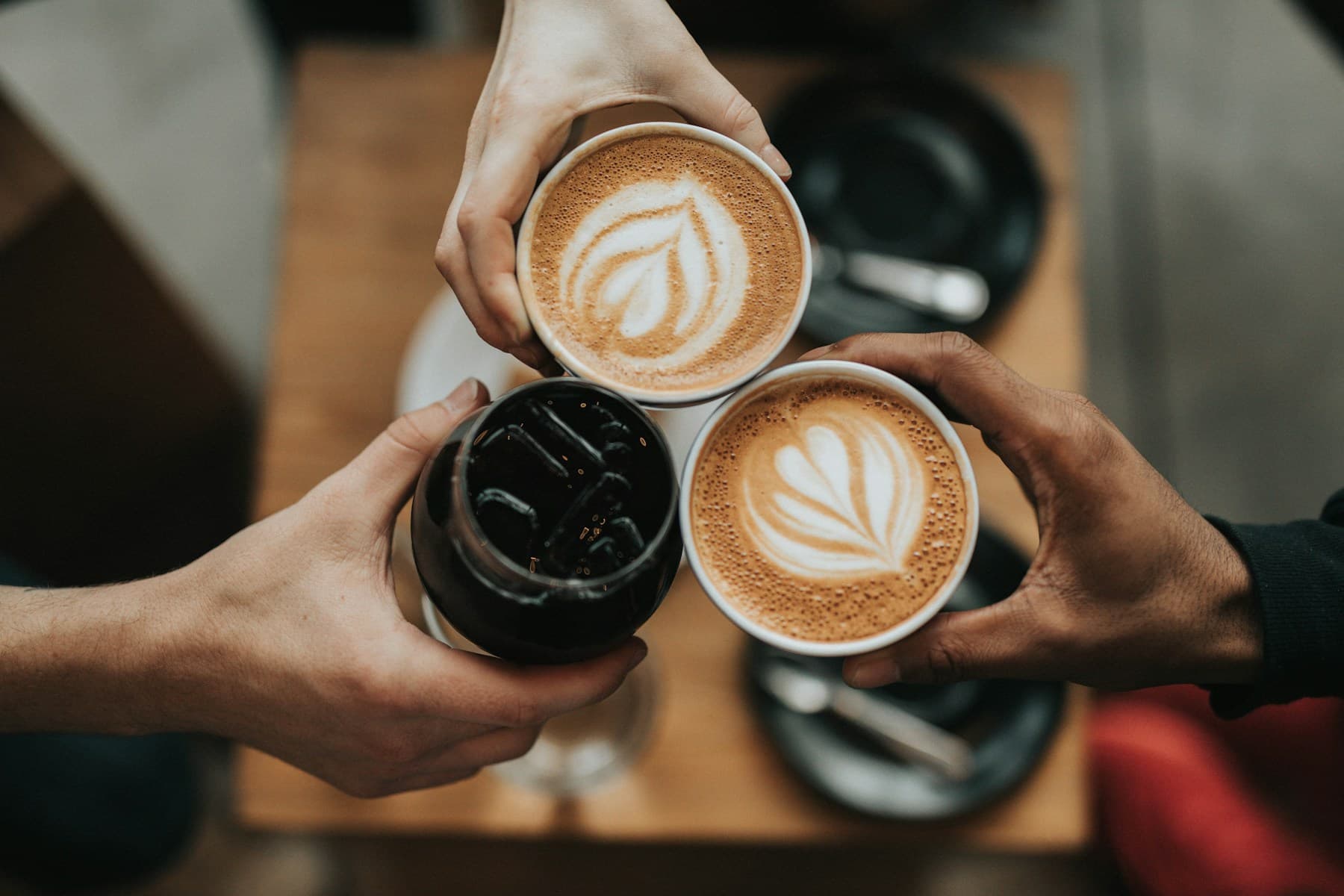 An overhead view of hands holding colorful coffee drinks, with no faces visible