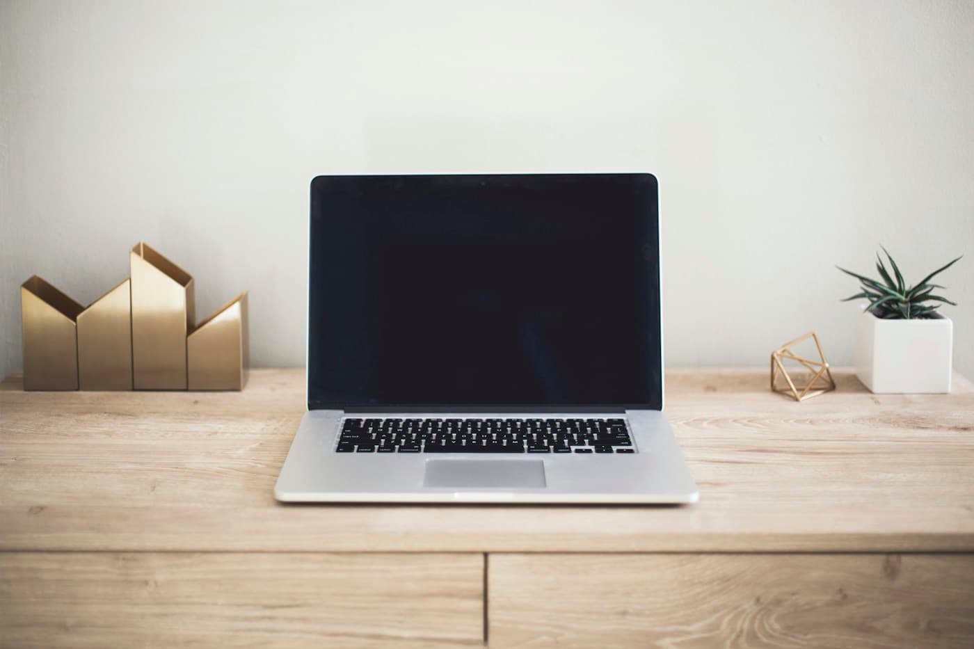 A laptop on a minimal wooden desk with a plant and geometric accessories
